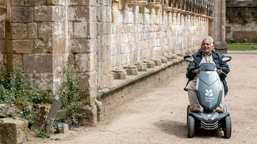 Older man using National Trust mobility scooter to explore the ancient abbey ruins on a summers day